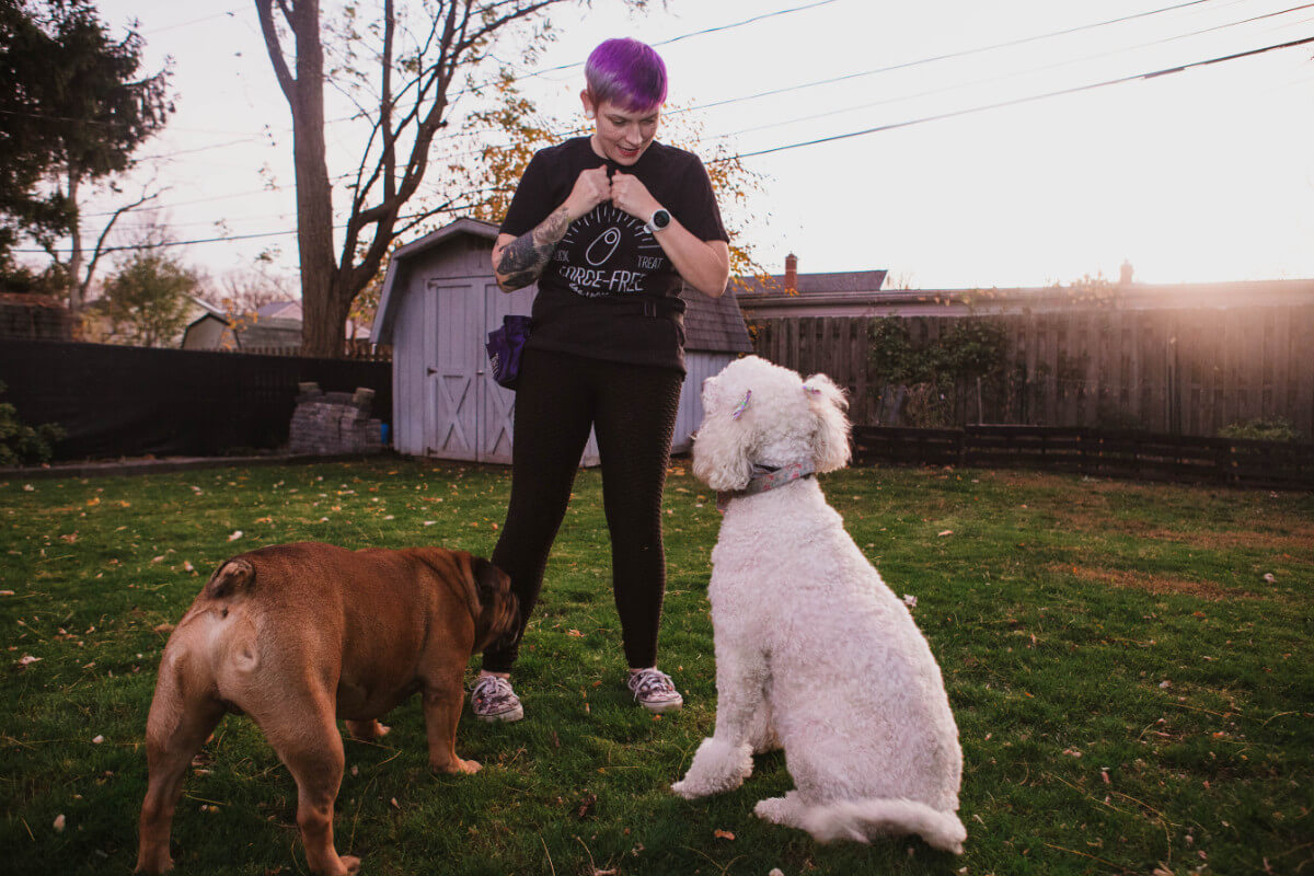 Tabitha teaching two dogs in front of her, a poodle and a bully mix, to sit.